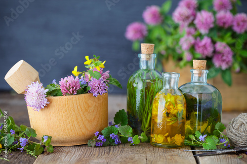 Bottles of tincture or infusion of healthy herbs  healing herbs and wooden mortar of flowers on rustic table. Herbal medicine.