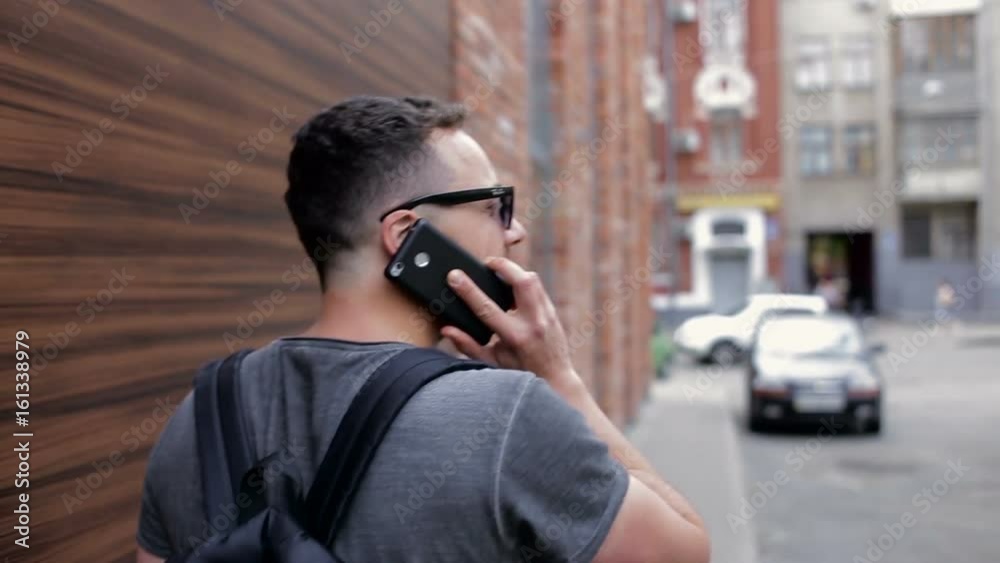 The guy is walking around the city near the brick wall and talking on the phone The guy is walking around the city near the brick wall and talking on the phone