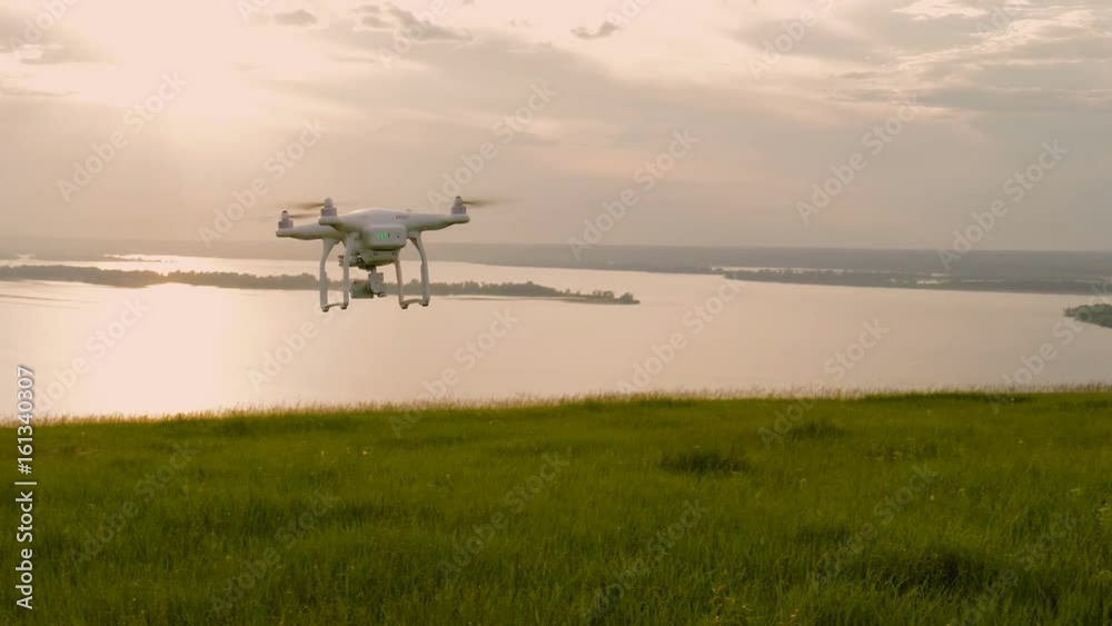 the white drone flying over the hill with green grass and is removed into the distance at sunset the white drone flying over the hill with green grass and is removed into the distance at sunset