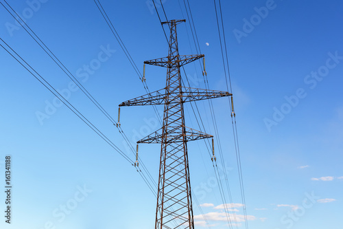 Electricity pylon silhouetted against blue sky background. High voltage tower