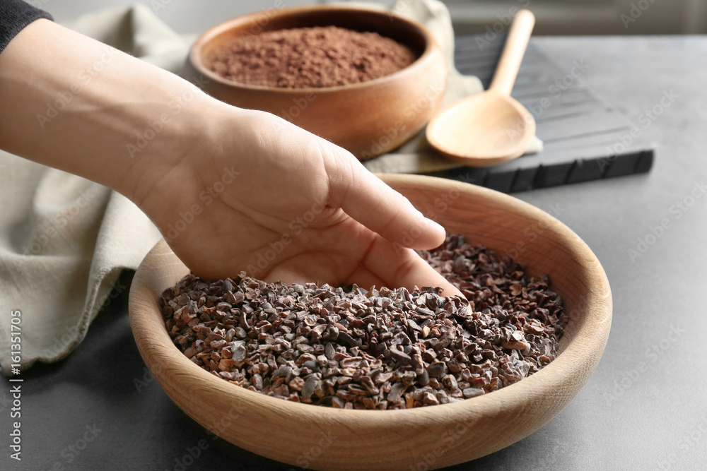 Human hand taking pile of cocoa nibs from wooden bowl Human hand taking pile of cocoa nibs from wooden bowl