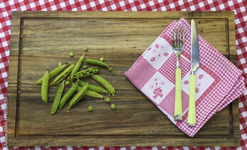 Peas and kitchen napkin on wooden board. Fork and knife on napkin.
