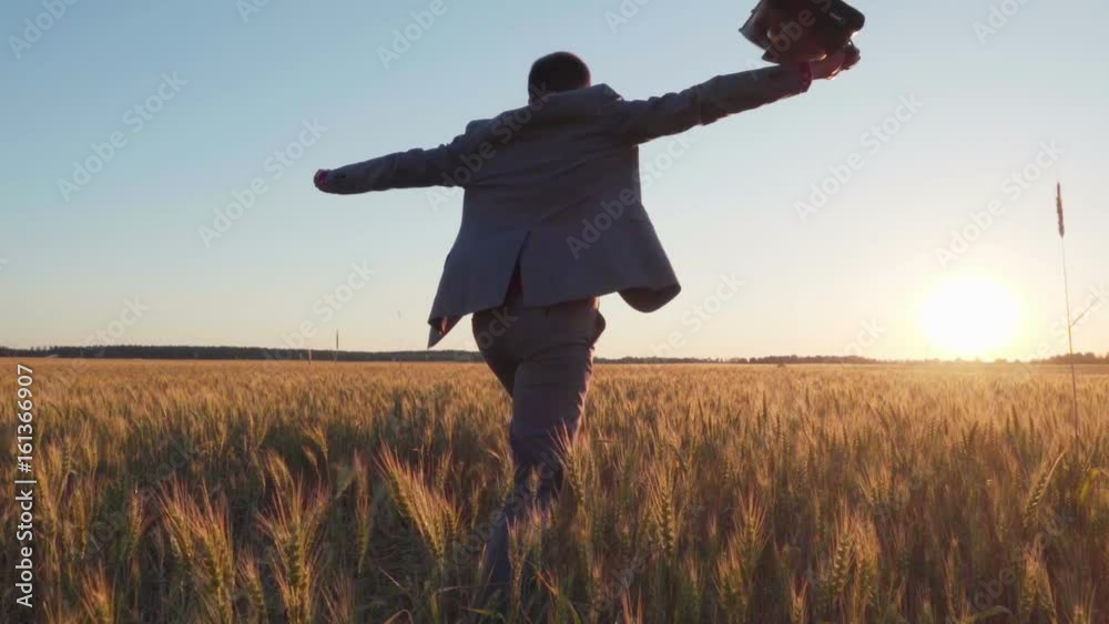 Happy free businessman with a briefcase running through the wheat field at sunset, back view, slow motion Happy free businessman with a briefcase running through the wheat field at sunset, back view, slow motion