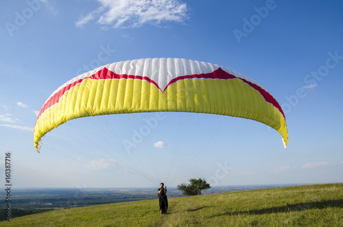 Closeup of paraglider wing on blue sky, man holding lines 