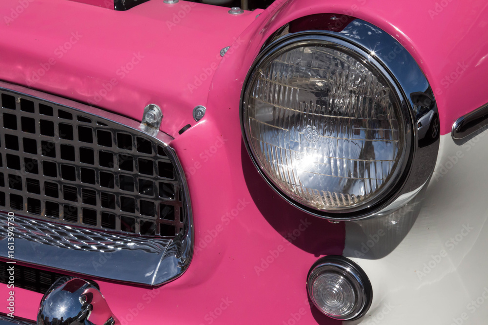 One headlight and grille on a pink and white classic car