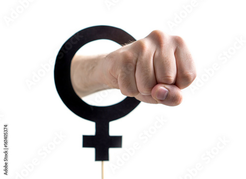 Male chauvinism, domestic violence or sexual equality concept. Also feminism, girl power or gender equality concept. Hand and fist through female symbol and sign cut from cardboard and wooden stick.