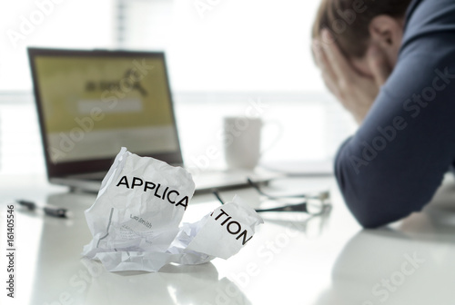 Frustration in job search. Unemployed man cant' find work. Jobless, sad, confused, worried and tired person holding hands on face. Ripped application paper on home office table. Employment concept.