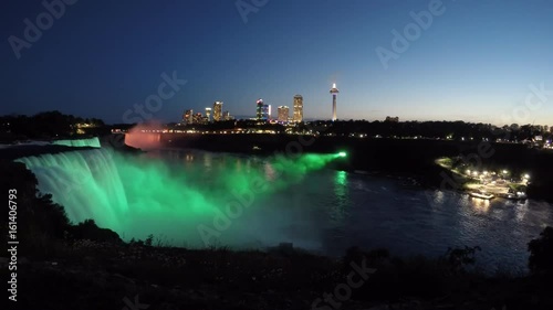 Niagara Falls colorful light illumination from New York State with Canadian skyline. Evening tour boat sailing into mist on Niagara River under fireworks. Time lapse