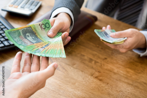 Businessman giving money (australian dollars) at working desk