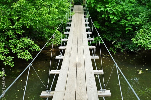 Fototapeta Naklejka Na Ścianę i Meble -  Small wood pedestrian suspension bridge with steel cables over a river in the woods