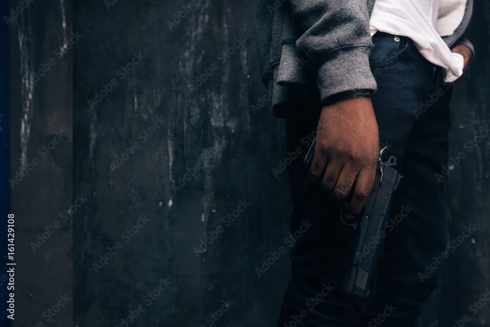 Unrecognizable armed black rapist closeup studio shoot. Gangster man with gun in hand on dark background. Outlaw, ghetto, murderer, robbery concept Unrecognizable armed black rapist closeup studio shoot. Gangster man with gun in hand on dark background. Outlaw, ghetto, murderer, robbery concept