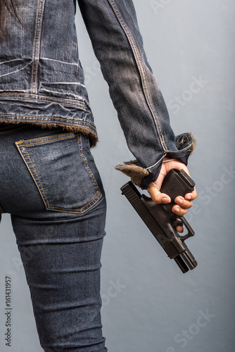 Woman in jeans is holding a gun in her hand.