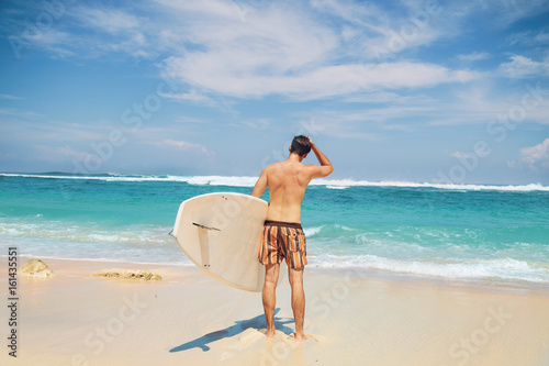 Young surfer guy with surfboard enjoying on the beach.