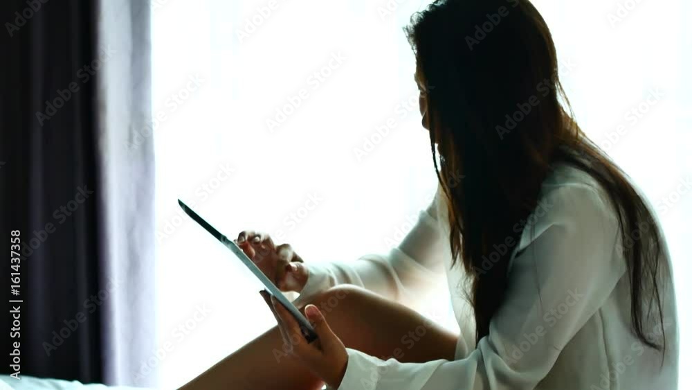 Asian woman use a tablet on the bed after wake up in weekend mornning.Use the tablet to read news, watch movies, or chat in relex and Communications, social media concept. Asian woman use a tablet on the bed after wake up in weekend mornning.Use the tablet to read news, watch movies, or chat in relex and Communications, social media concept.