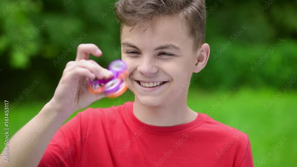 Child having fun outdoors with Spinner. Teen boy showing skills by flicking fidget spinners with finger. Teenager in the summer park.