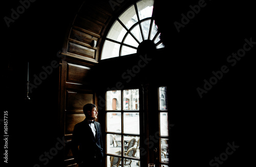 Thoughtful man in black suit stands before the window