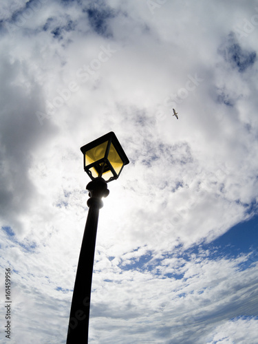 Vintage street lamp in front of blue sky with white clouds and gull in the distance