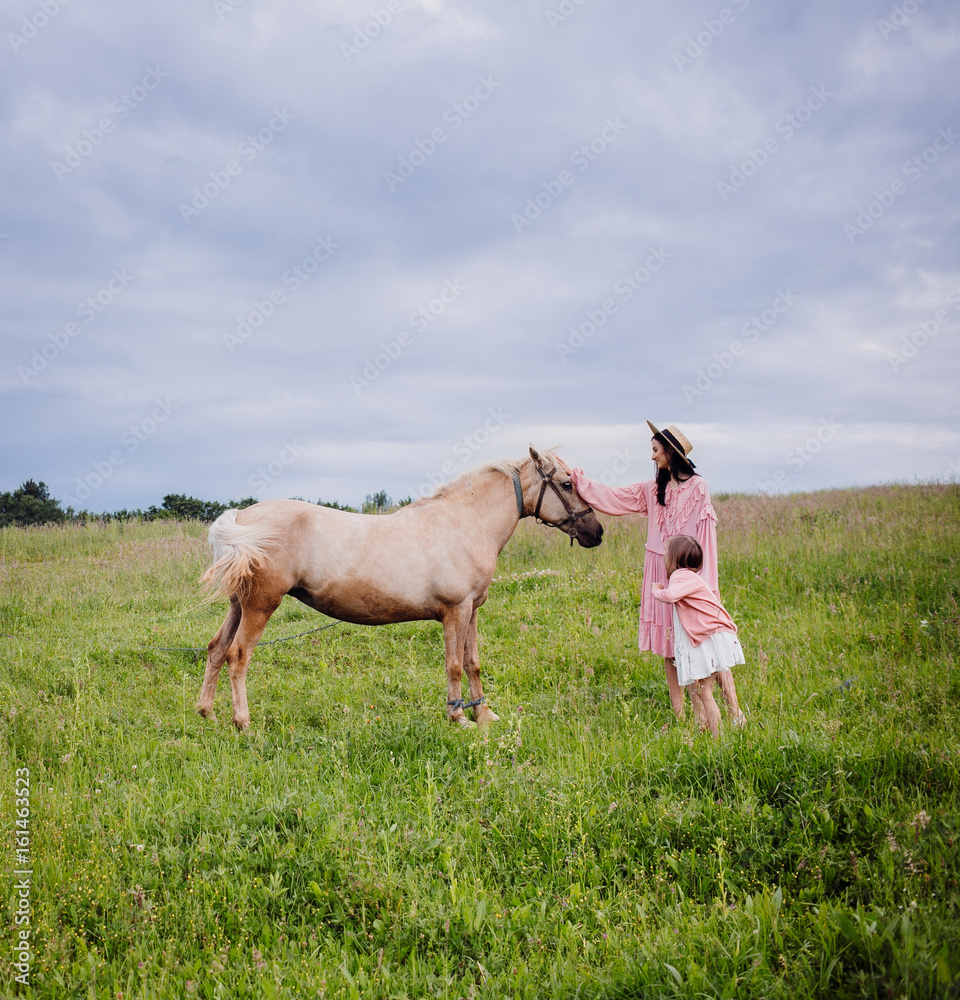 Mother and daughter stand on the field before a horse Mother and daughter stand on the field before a horse