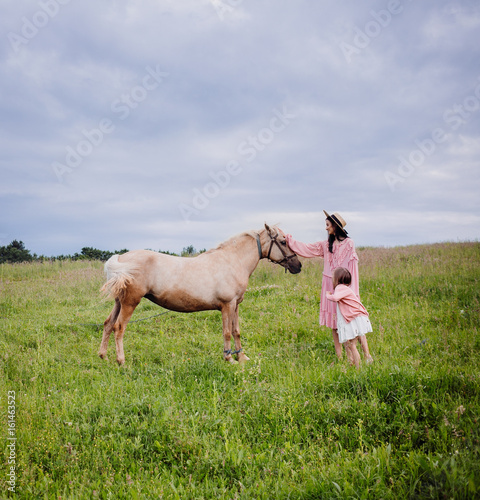Mother and daughter stand on the field before a horse © pyrozenko13