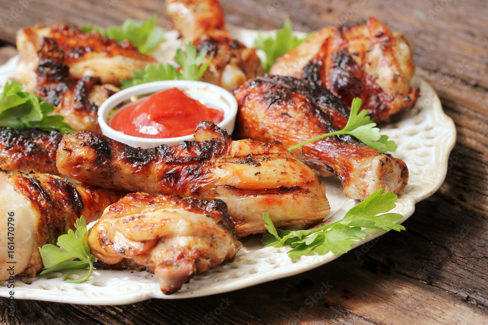 Grilled chicken legs on wooden table served on white plate with coriander