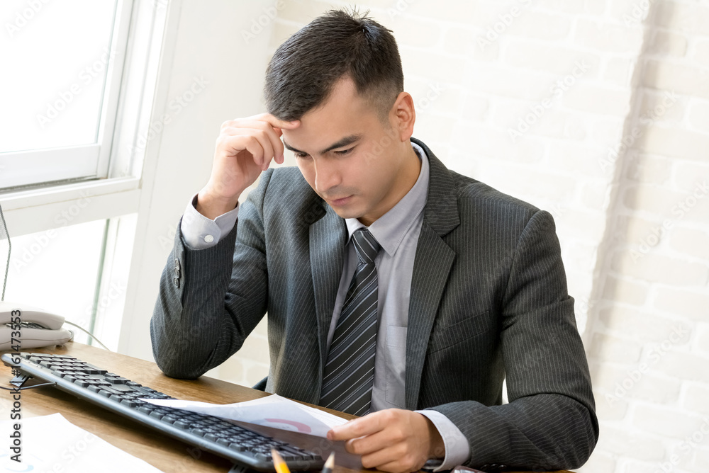 Businessman with hand on temple getting serious while reading document Businessman with hand on temple getting serious while reading document