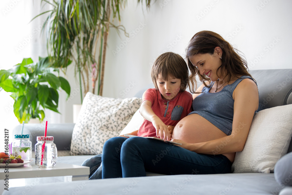 Young pregnant woman, reading a book at home to her boy Young pregnant woman, reading a book at home to her boy