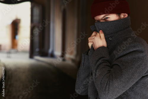 Man hides himself behind the collar posing in grey coat