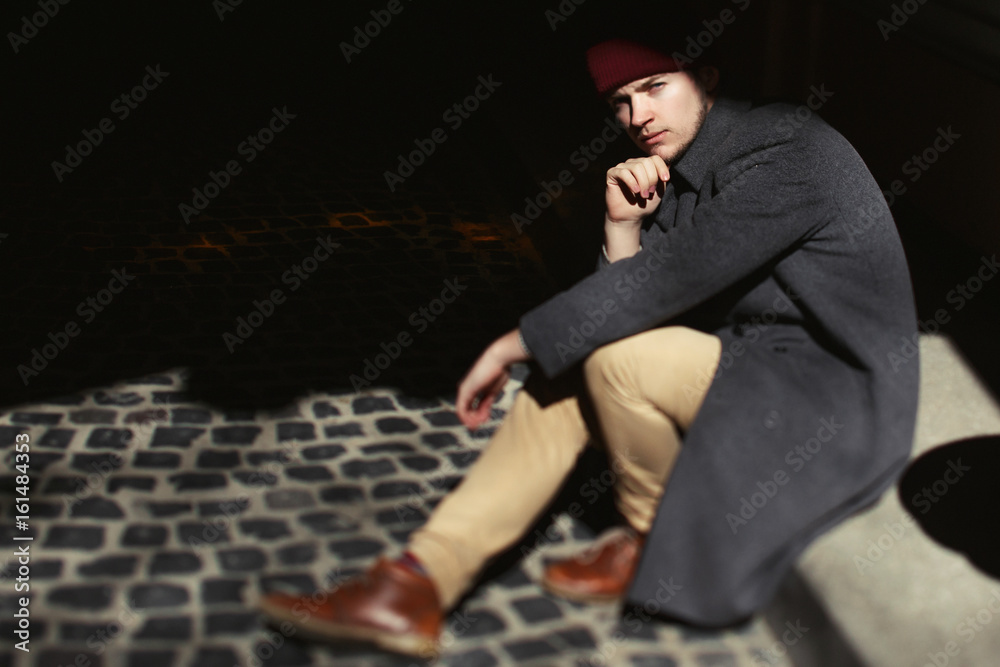 Man in grey coat sits in the shadow on the pavement