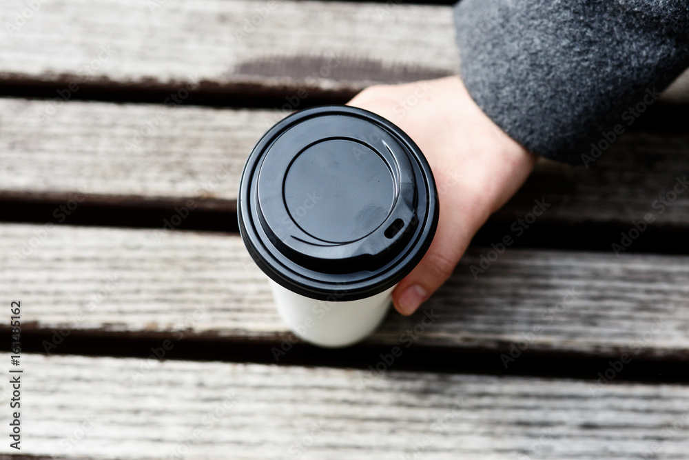Look from above at man holding paper cup of coffee on the wooden bench Look from above at man holding paper cup of coffee on the wooden bench