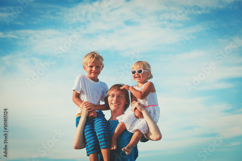 happy father with two kids on shoulders at sky