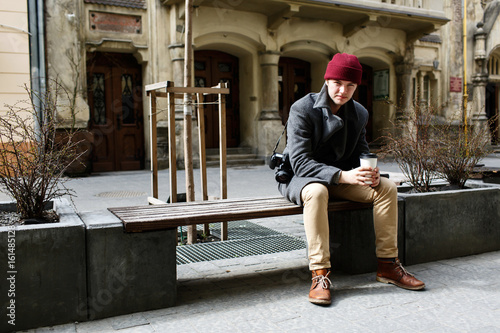 Boy with cup of coffee sits on the bench