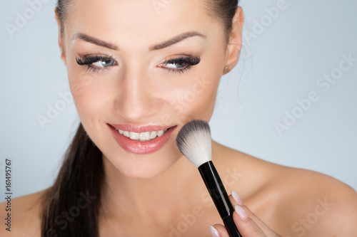 Happy beautiful woman applying face powder