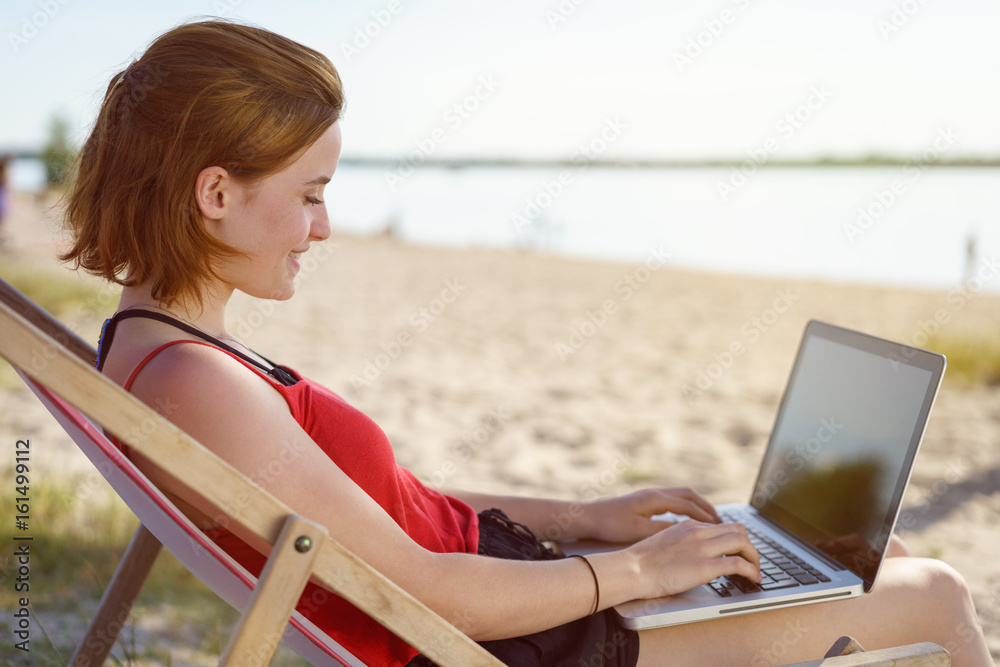 Young woman typing on her laptop on a sandy beach