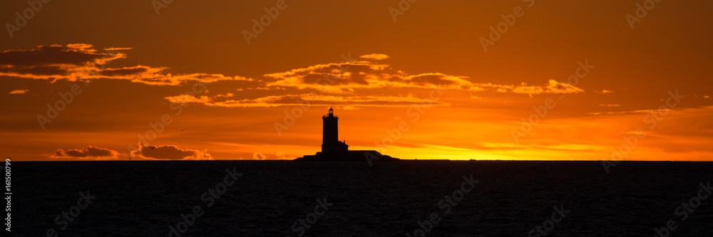 Silhouette of a lighthouse against the background of an orange sky at sunset