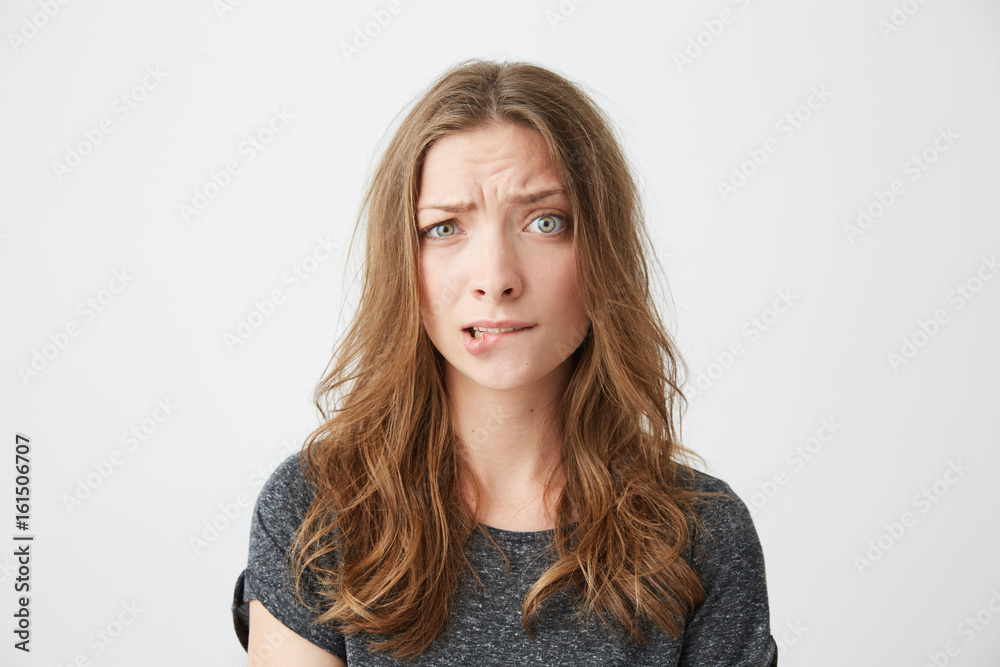 Nervous young beautiful girl looking at camera frowning biting lip over white background. Nervous young beautiful girl looking at camera frowning biting lip over white background.
