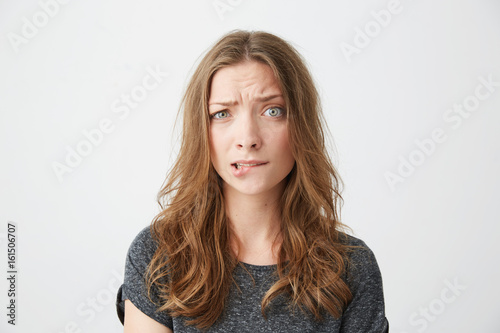 Nervous young beautiful girl looking at camera frowning biting lip over white background.