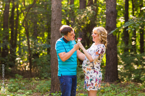 Pregnancy, family, happiness and fun concept - Man and pregnant woman have fun with candy in the park