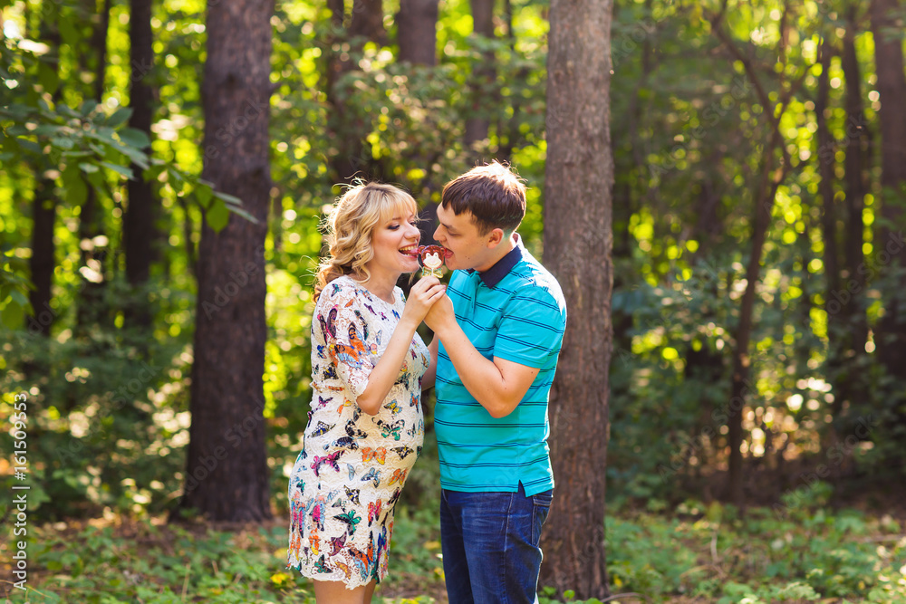 Pregnancy, family, happiness and fun concept - Man and pregnant woman have fun with candy in the park Pregnancy, family, happiness and fun concept - Man and pregnant woman have fun with candy in the park