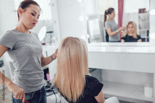 Hair-stylist by hair combs girl hair in beauty studio.