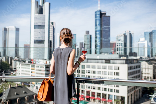 Young businesswoman enjoying wine on the terrace with great view on the skyscrapers in Frankfurt city