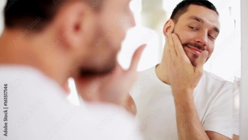 happy man applying aftershave to face at bathroom happy man applying aftershave to face at bathroom