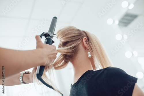 Hair stylist makes a curls for a girl, using hair styling. Hairdresser at work.