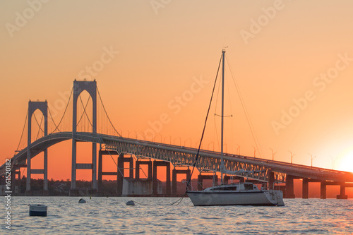 Sunset over Newport Bridge in Newport, Rhode Island.  There is a sailboat moored in front of the Newport Pell Bridge photo