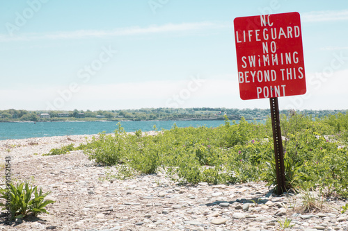 A red sign warns beach goers that there is no lifeguard, no swimming beyond this point