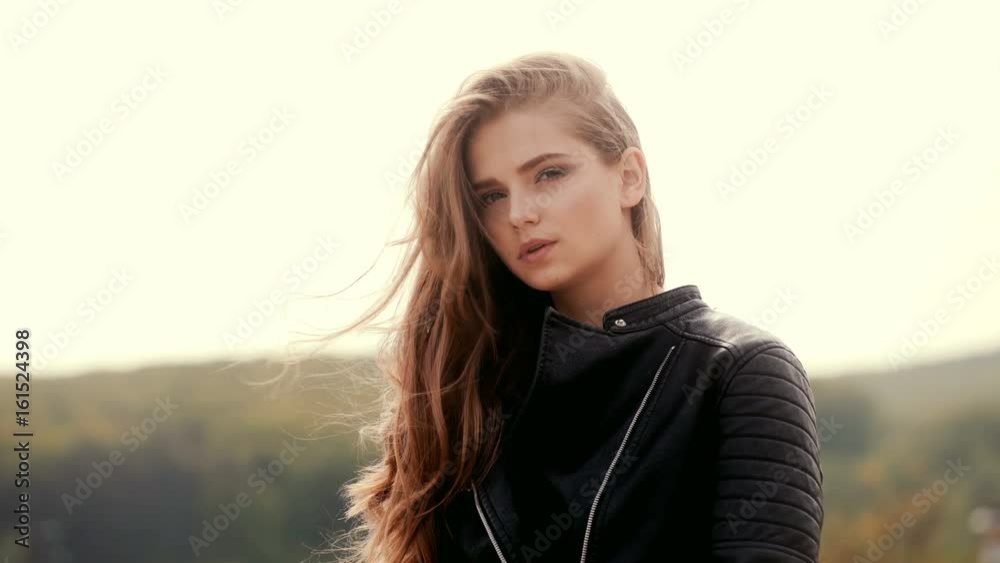 Blonde girl with wavy hair in black jacket against the background of mountains. Beautiful sexy young woman with makeup and beautiful romantic look. Attractive female face model. Long hair, clean face Blonde girl with wavy hair in black jacket against the background of mountains. Beautiful sexy young woman with makeup and beautiful romantic look. Attractive female face model. Long hair, clean face