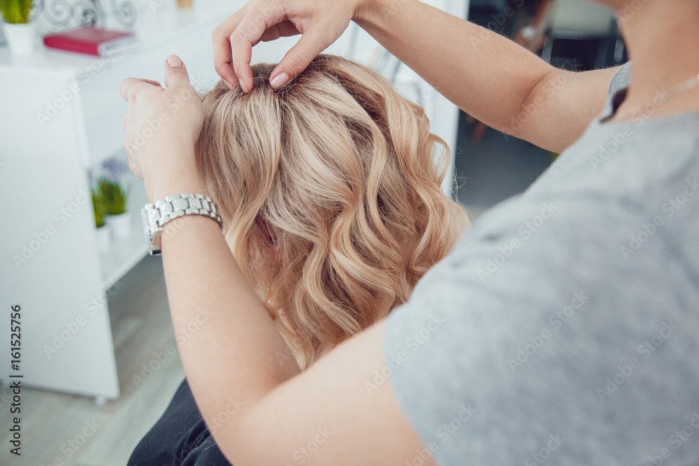 Naklejka premium Hair stylist makes a curls for a girl, using hair styling. Hairdresser at work.