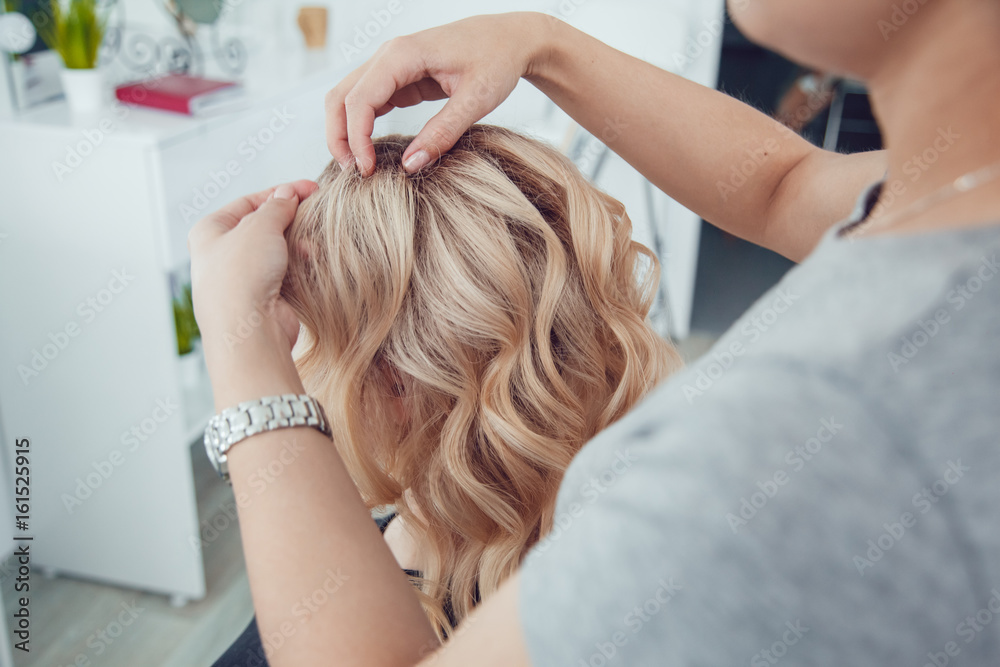 Fototapeta premium Hair stylist makes a curls for a girl, using hair styling. Hairdresser at work.