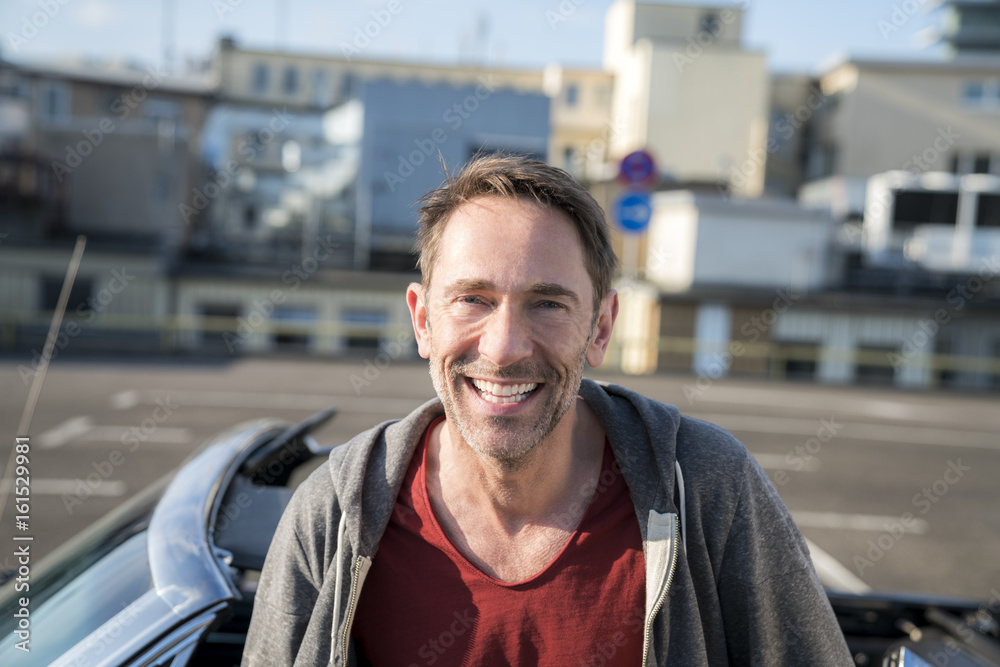 Portrait of laughing mature man with stubble in front of his sports car Portrait of laughing mature man with stubble in front of his sports car
