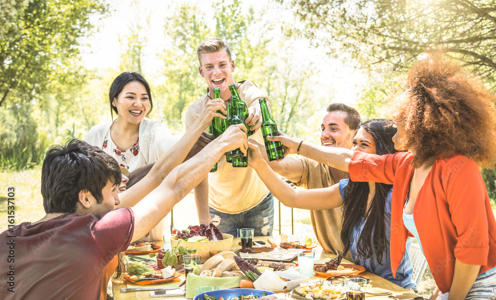 Obraz premium Young multiracial friends toasting at barbecue garden party - Friendship concept with happy people having fun at backyard bbq summer camp - Food and drinks fancy picnic lunch - Focus on beer bottles