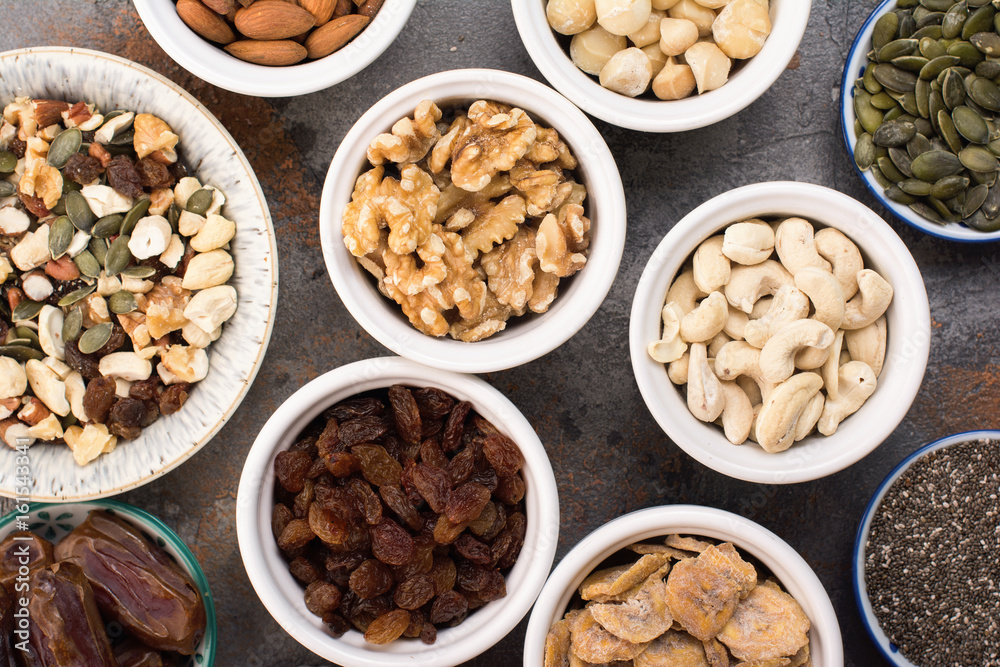 Ingredients for homemade paleo granola, different nuts and raisins, dates, seed on the grey stone background, top view Ingredients for homemade paleo granola, different nuts and raisins, dates, seed on the grey stone background, top view